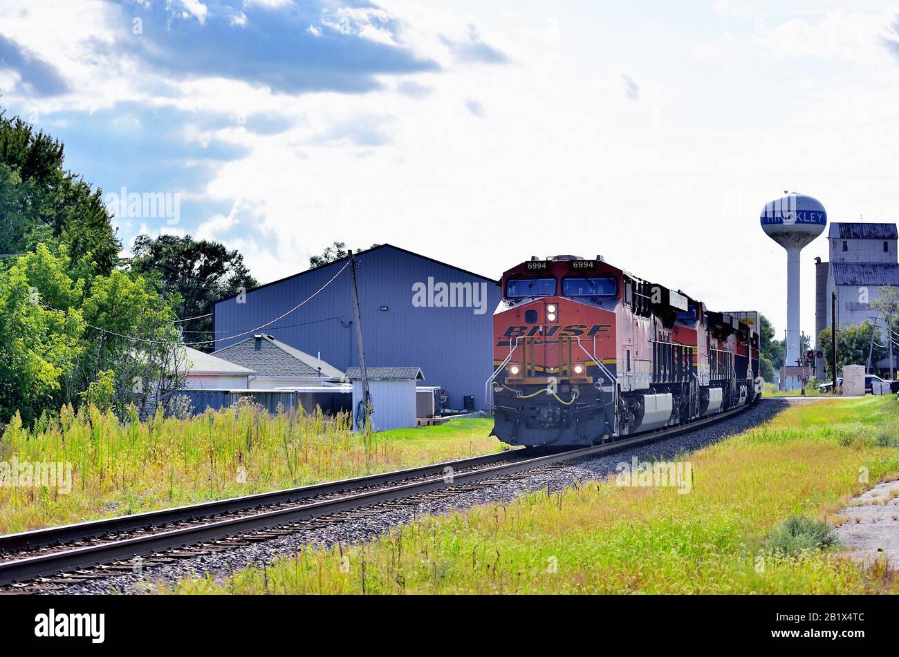 Hinckley, Illinois, USA. Four Burlington Northern Santa Fe locomotives lead a freight train past a old grain elevator and water tower. Stock Photo