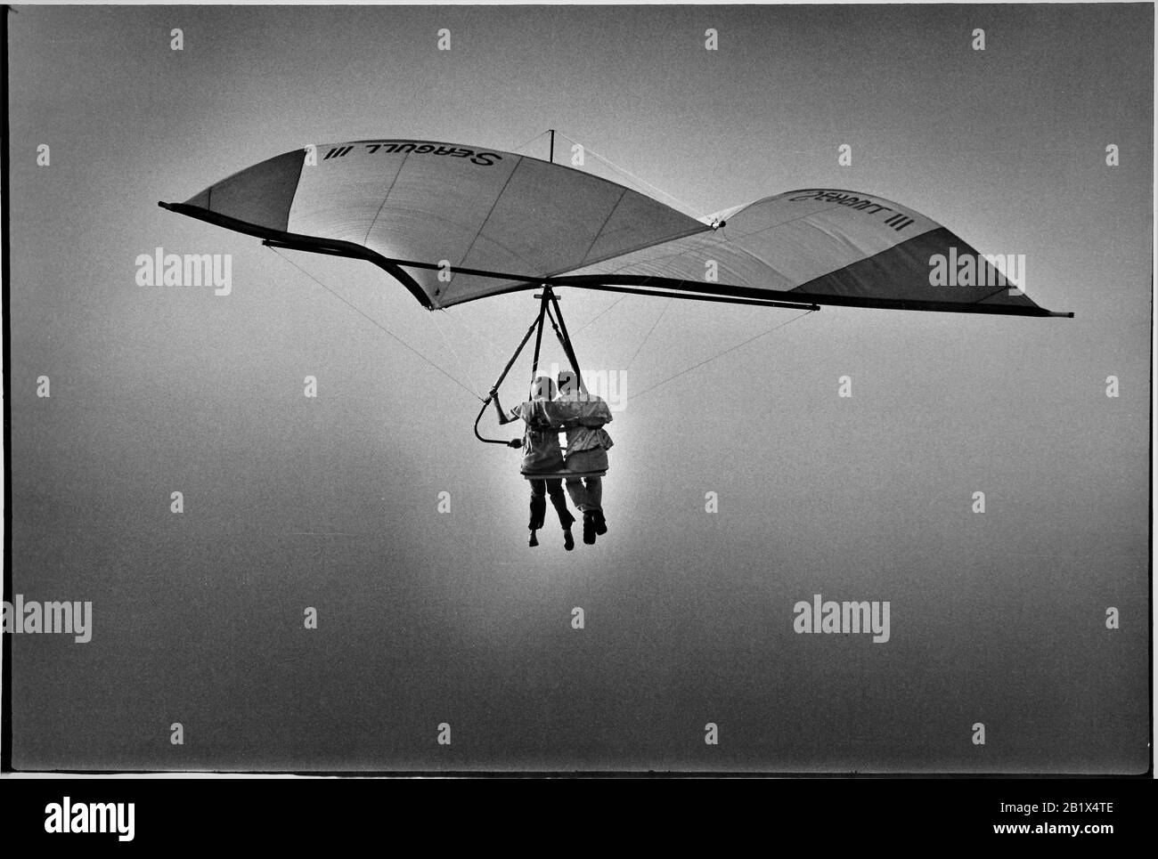 man pilot and his passenger girlfriend on a 1970's hang glider together over the ocean in San Pedro CA USA at altitude Stock Photo