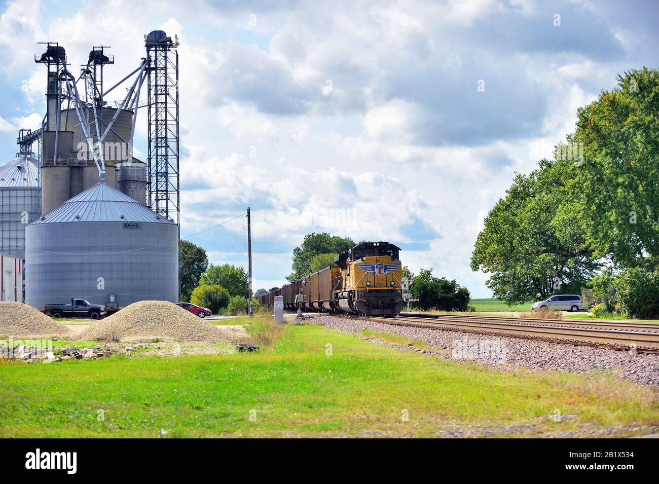 Malta, Illinois, USA. A helper locomotive unit assists a Union Pacific coal train, lead by three locomotive units, as it passes a farming cooperative. Stock Photo