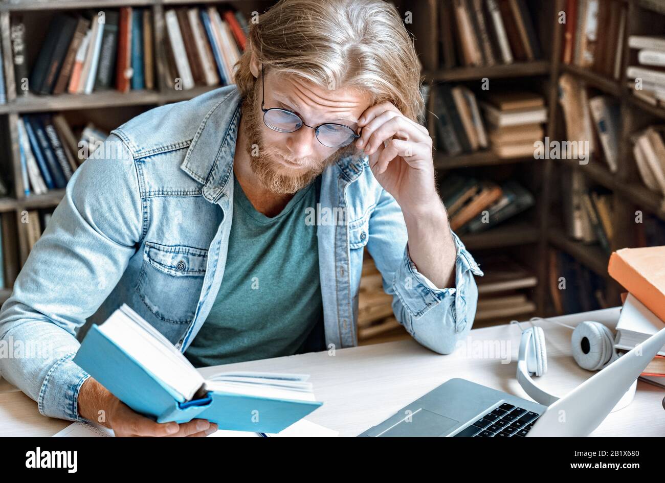 Young focused man library desk surprised look at open book volume copy space. Stock Photo