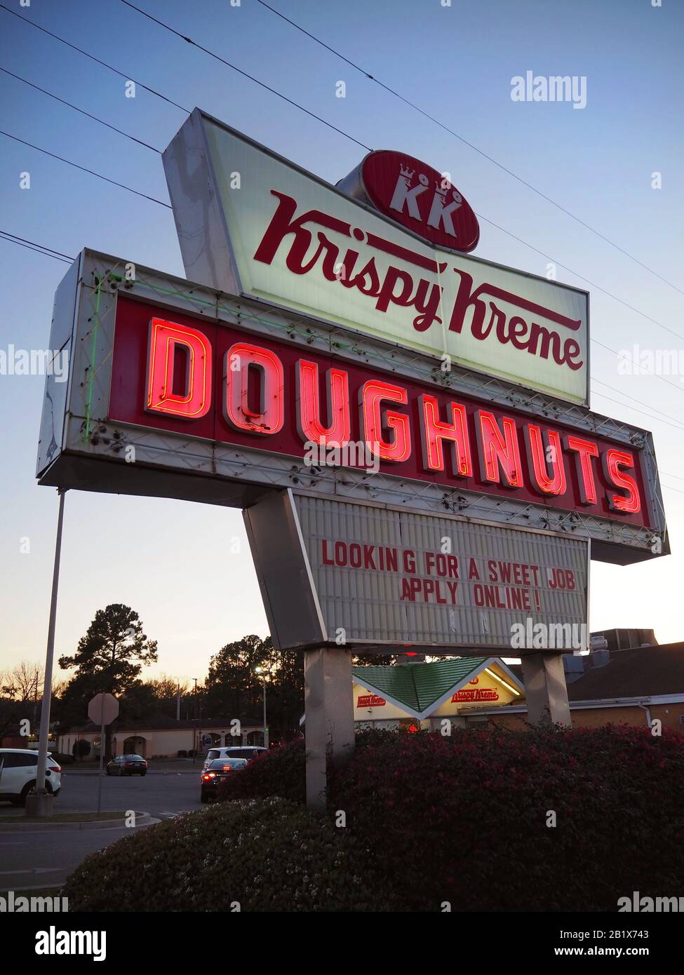 SAVANNAH, GA - FEBRUARY 22, 2020: A red and white lighted neon sign for Krispy Kreme donuts glows on a street corner at dusk in Savannah, Georgia. Stock Photo