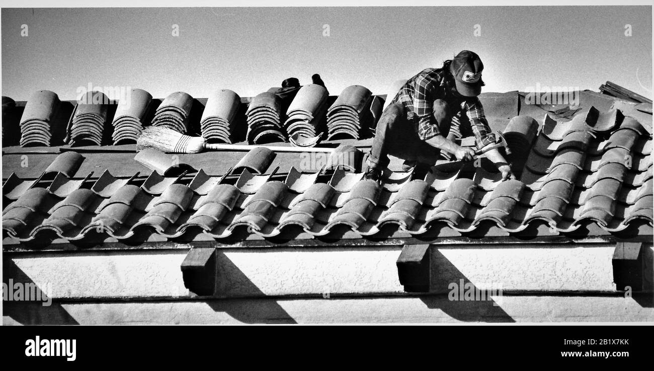 Hispanic Mexican man installing fire resistance mission style tiles on roof in fire zone of California Stock Photo