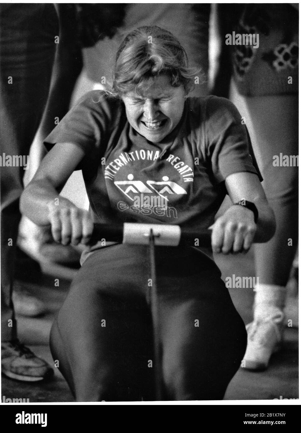 Young Caucasian woman working out on rowing machine to improve her single skull times in Long Beach stadium Stock Photo