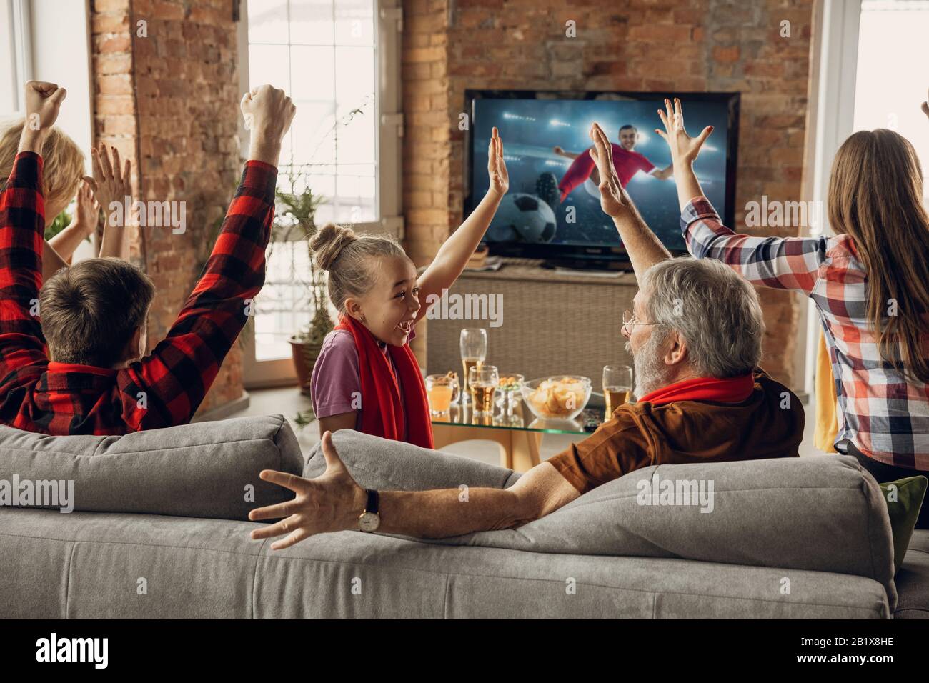 Victory. Excited, happy family watching soccer, football match,  championship on the couch at home. Fans emotional cheering for favourite  national team. Daughter, dad and grandpa. Sport, TV, having fun Stock Photo  -