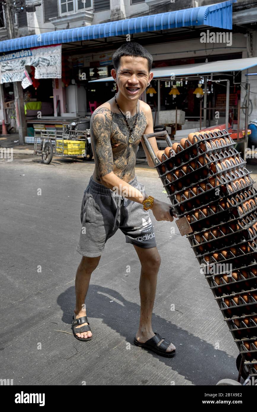 Tattooed man transporting eggs with a hand cart. Thailand street scene Stock Photo