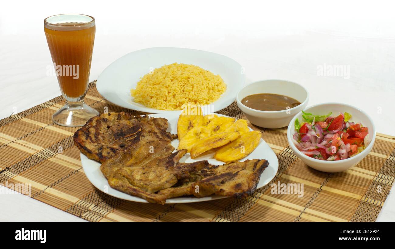 White plate with pork chop accompanied by fried banana, salad and yellow rice with a glass cup with lemonade on white background Stock Photo