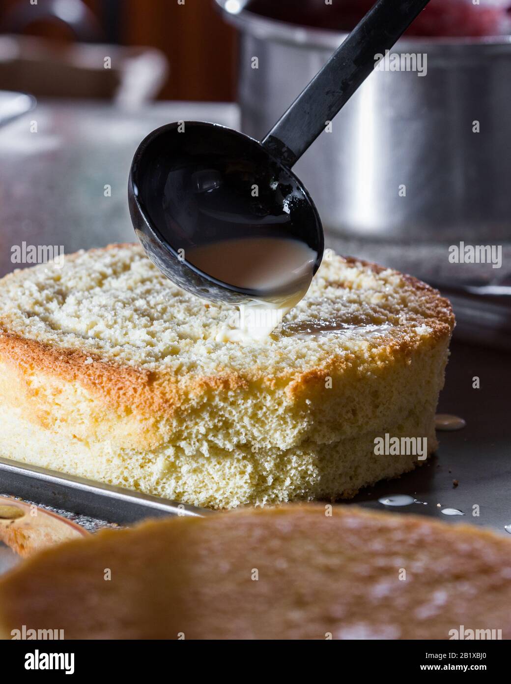 close up of a ladle pouring evaporated milk onto a fresh baked vanilla cake  layer to add moisture Stock Photo - Alamy