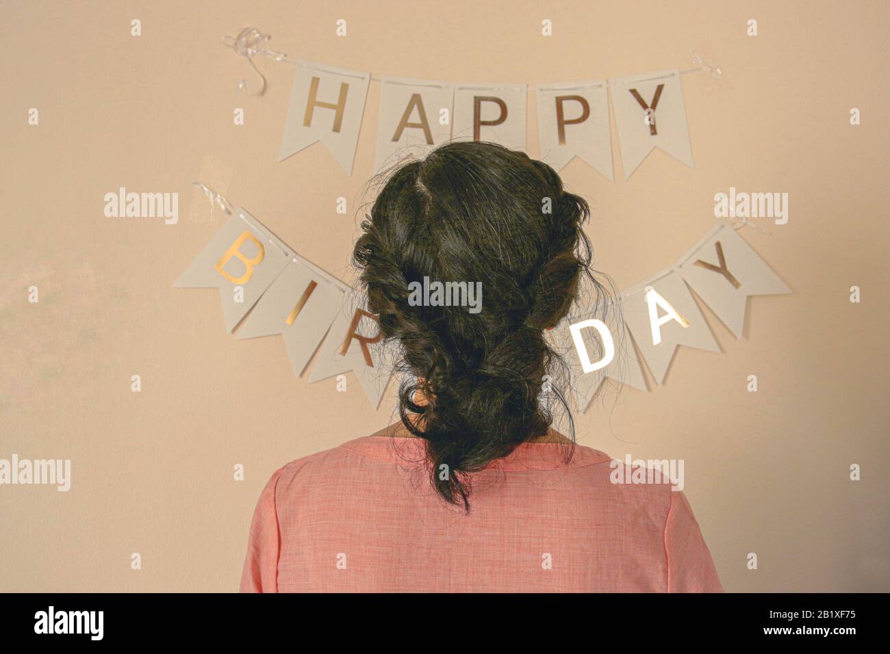 Unrecognizable woman with braided hair standing before a Happy Birthday buntings shot in pastel pink tones to create a cute and elegant birthday theme Stock Photo