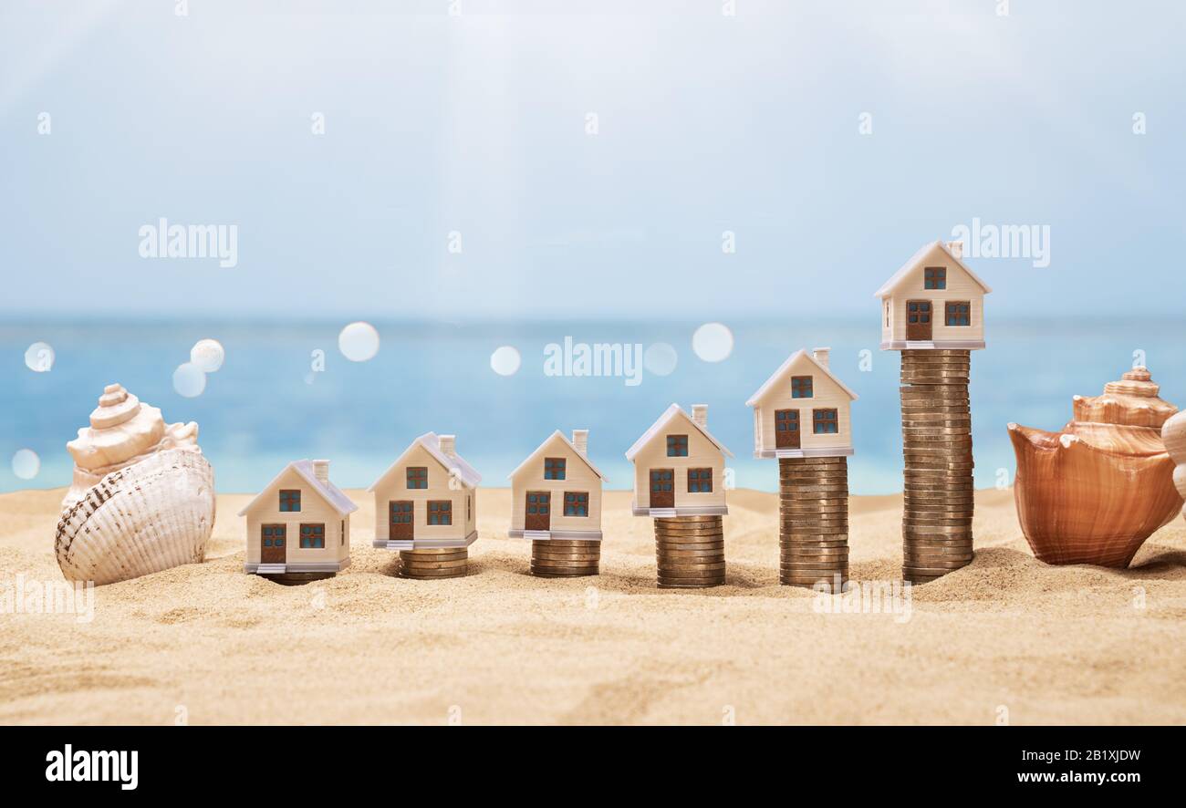 House Models Arranged On Stacked Coins At Sunny Beach Stock Photo