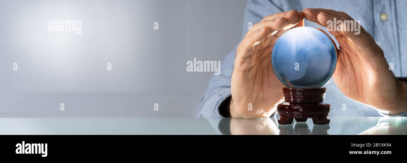 Midsection Of Businessman Covering Crystal Ball At Wooden Table Stock Photo