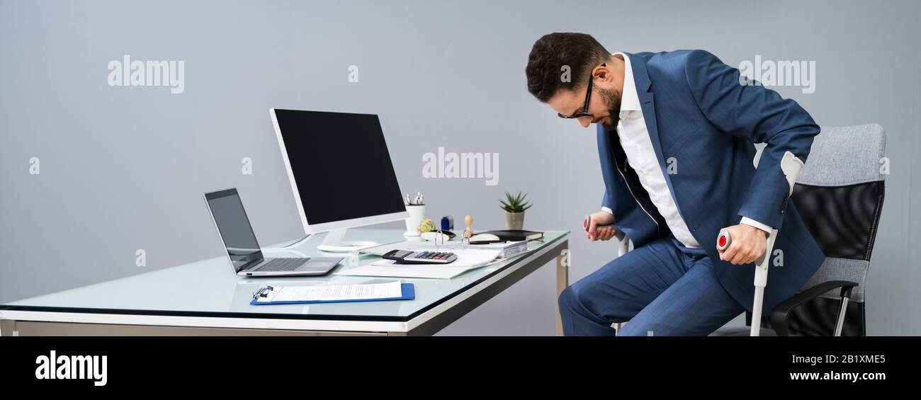 Man With Broken Leg Using Crutches To Get Up From Chair In Office Stock