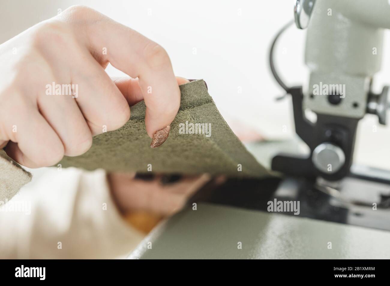 Young white woman stitching leather using a sewing machine Stock Photo