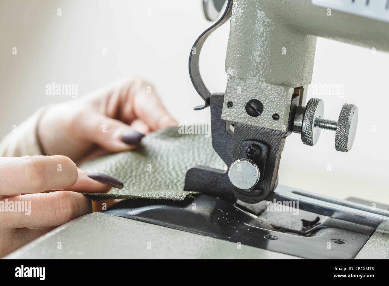 Young white woman stitching leather using a sewing machine Stock Photo