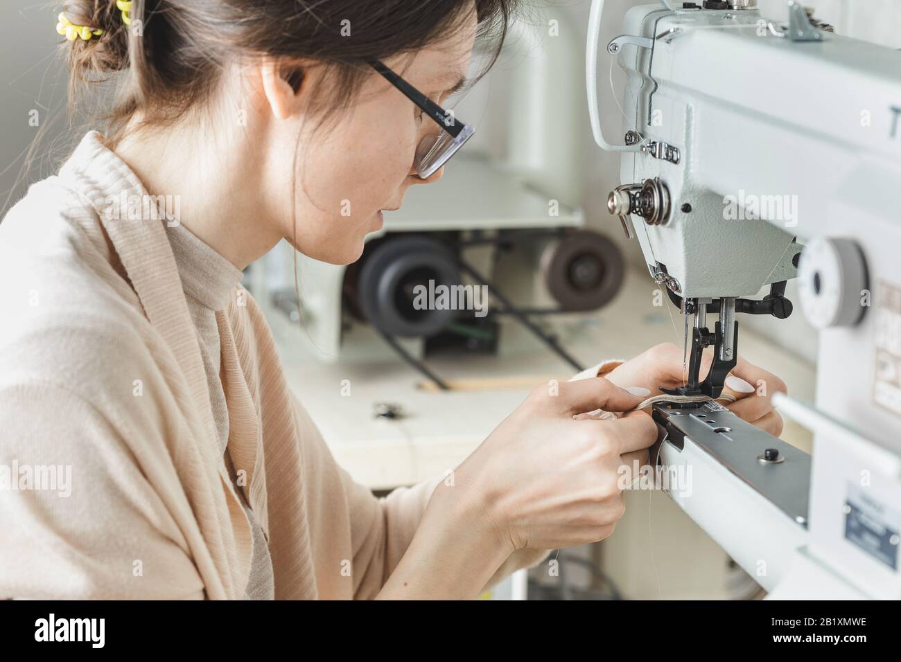 Young white woman stitching leather using a sewing machine Stock Photo