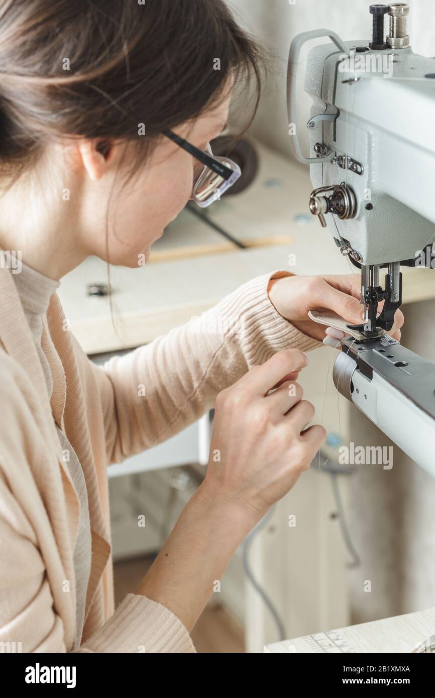 Young white woman stitching leather using a sewing machine Stock Photo