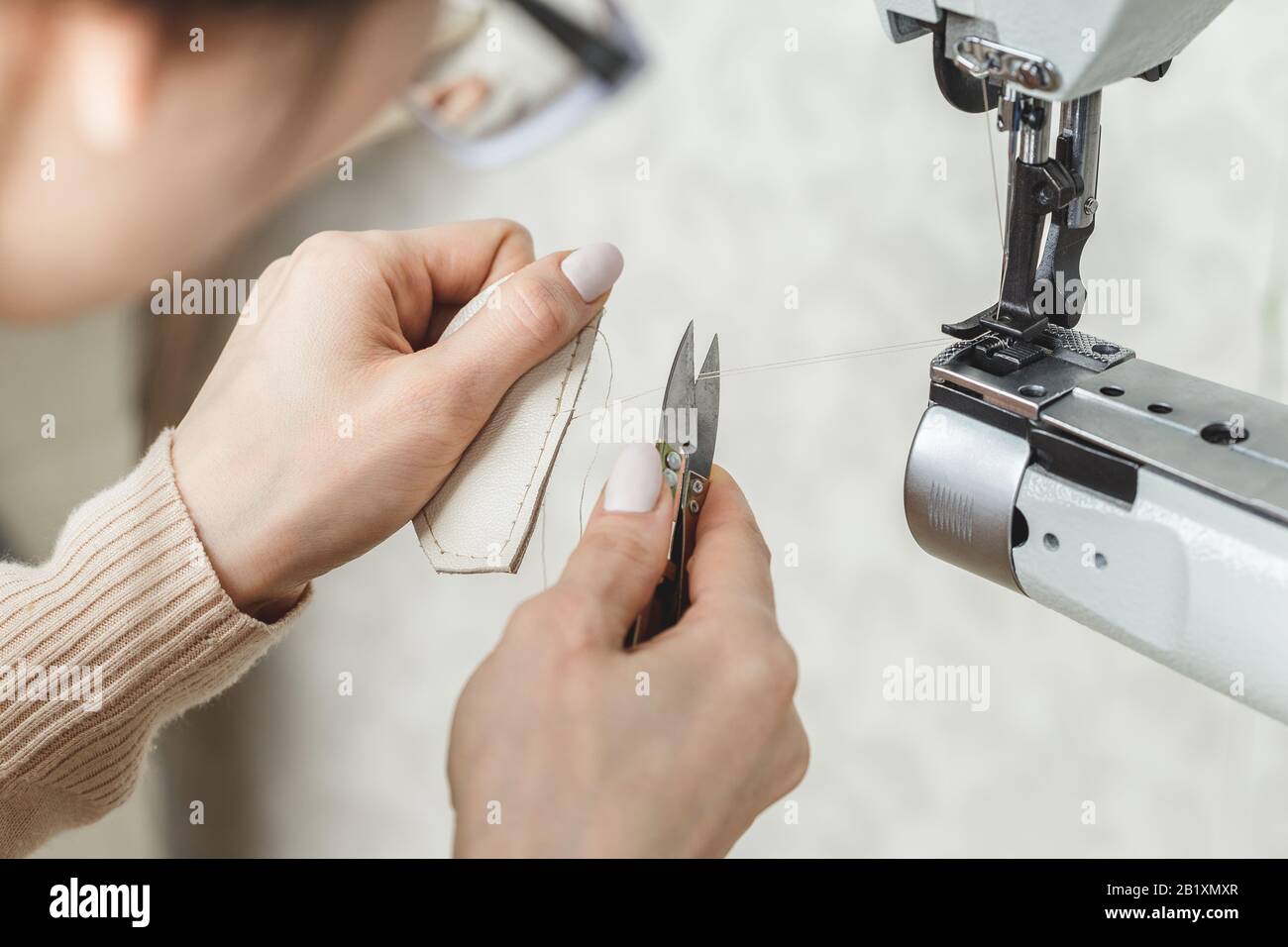 Young white woman stitching leather using a sewing machine Stock Photo