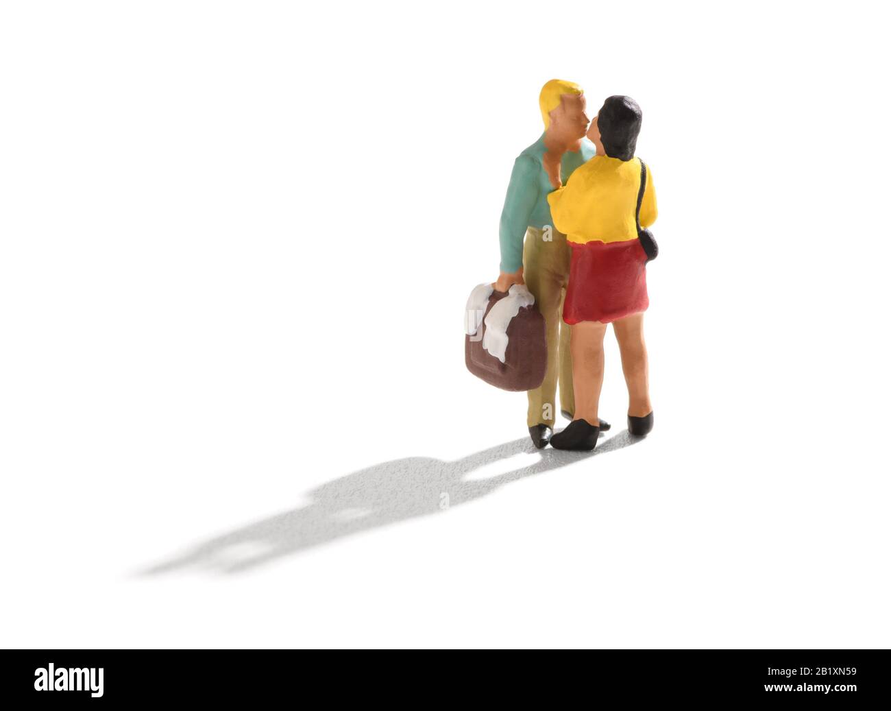 Small miniature couple, man and woman in casual clothes, standing and kissing. The man holding a bag or a suitcase in his hand. Isolated on white back Stock Photo