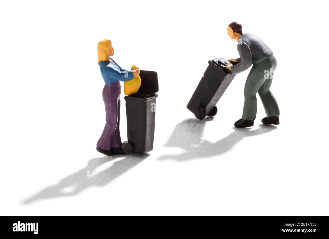 Two miniature people using rubbish bins with a housewife putting out a bag of waste and a garbage man wheeling one along over white with shadow Stock Photo