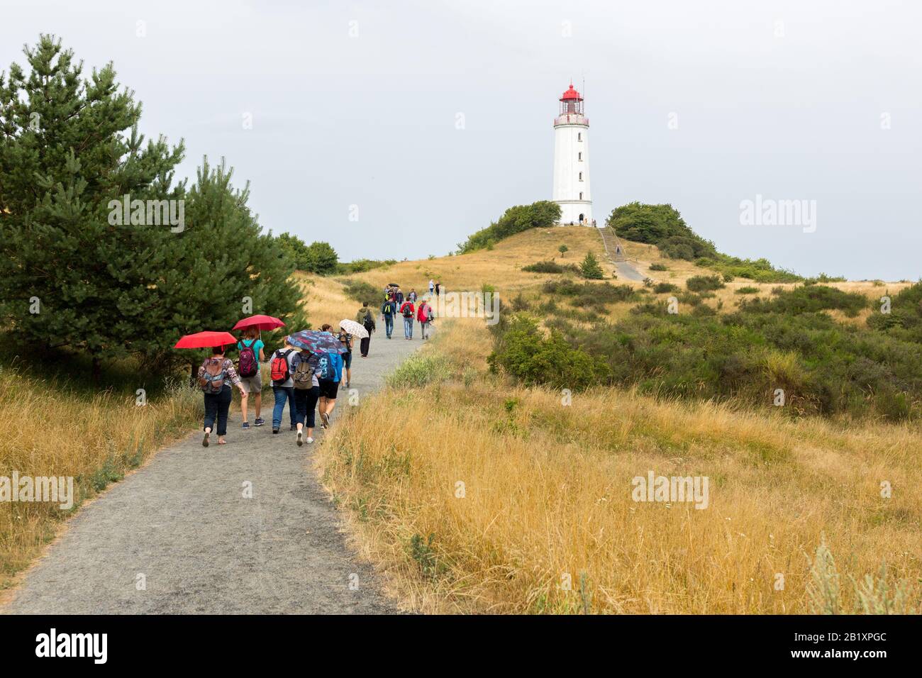 Historic Dornbusch lighthouse on Hiddensee Island (baltic sea) on a rainy day. Tourists with umbrellas walking towards the lighthouse. Stock Photo