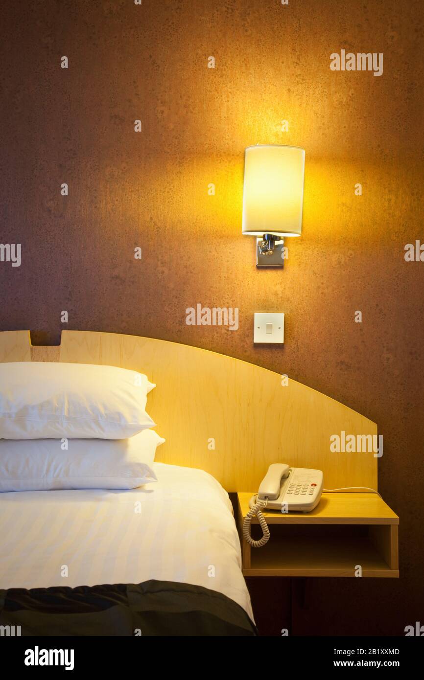 Illuminated hotel room bed at night with bedside telephone Stock Photo