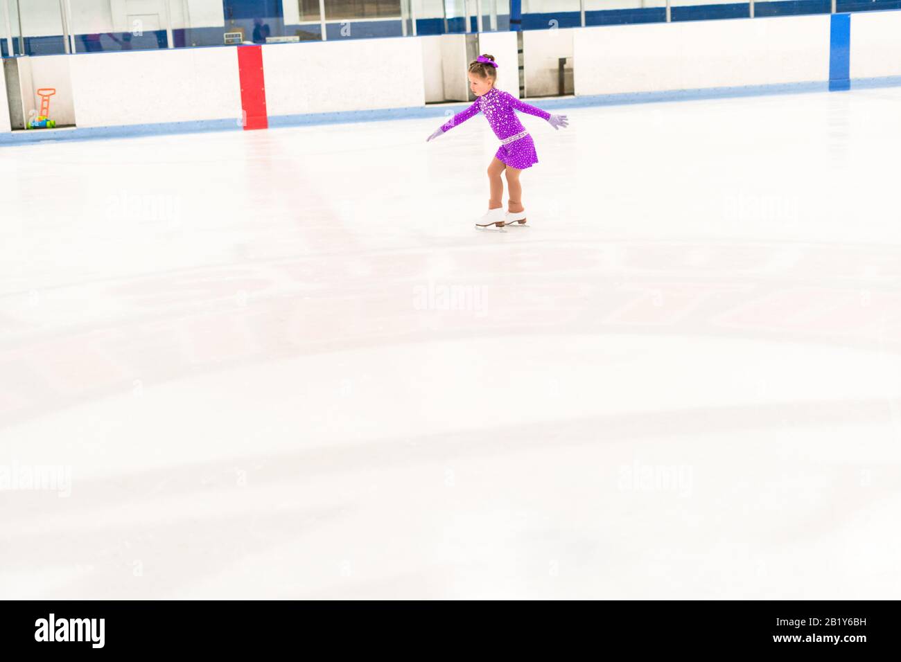 Little girl practicing figure skating in a purple dress with crystals