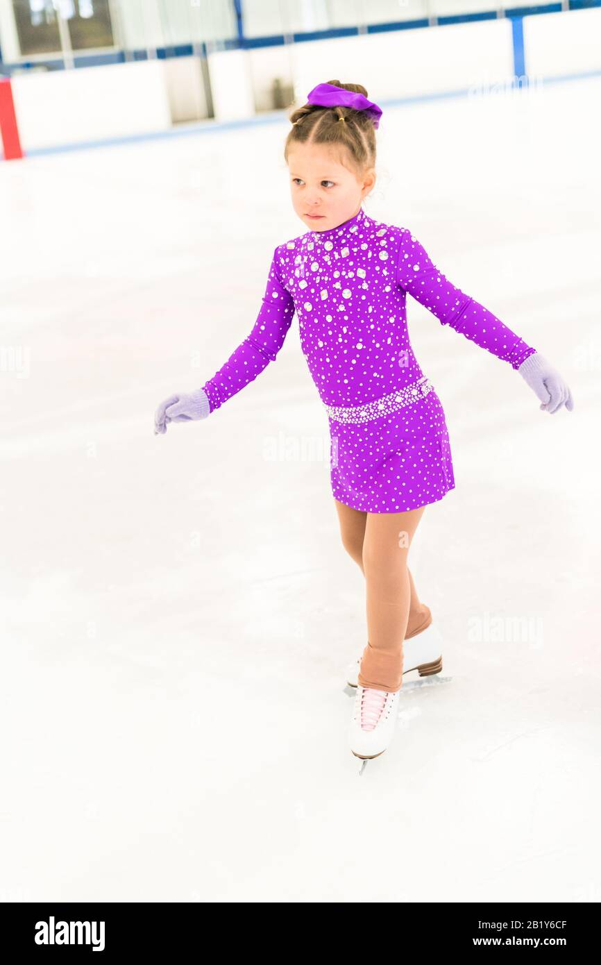 Little girl practicing figure skating in a purple dress with crystals
