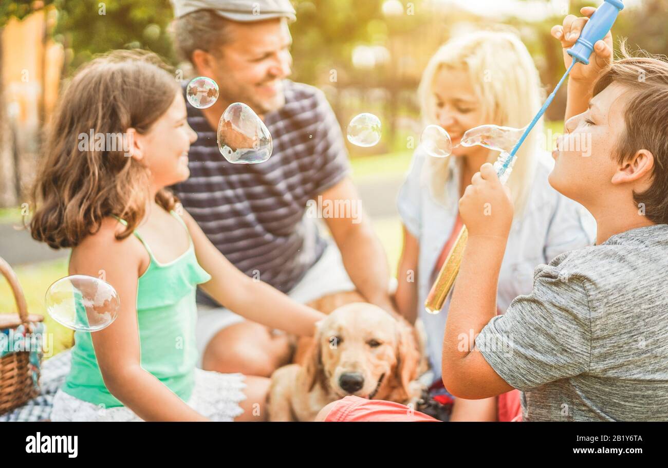 Happy family doing picnic in nature outdoor - Young parents having fun with children and their dog in summer time laughing, playing together with soap Stock Photo
