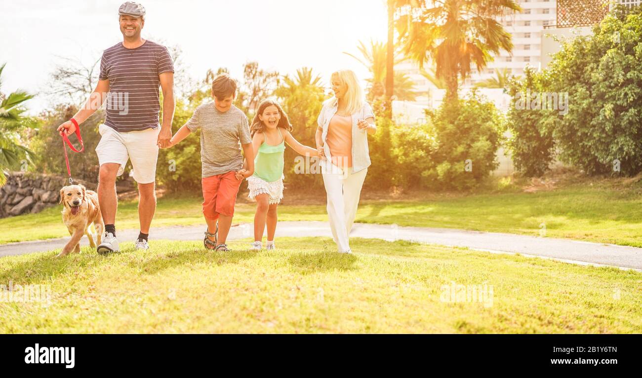 Happy family walking around public park during sunny day - Parents and children having fun with their dog in summer time - Vacation, holiday, positive Stock Photo