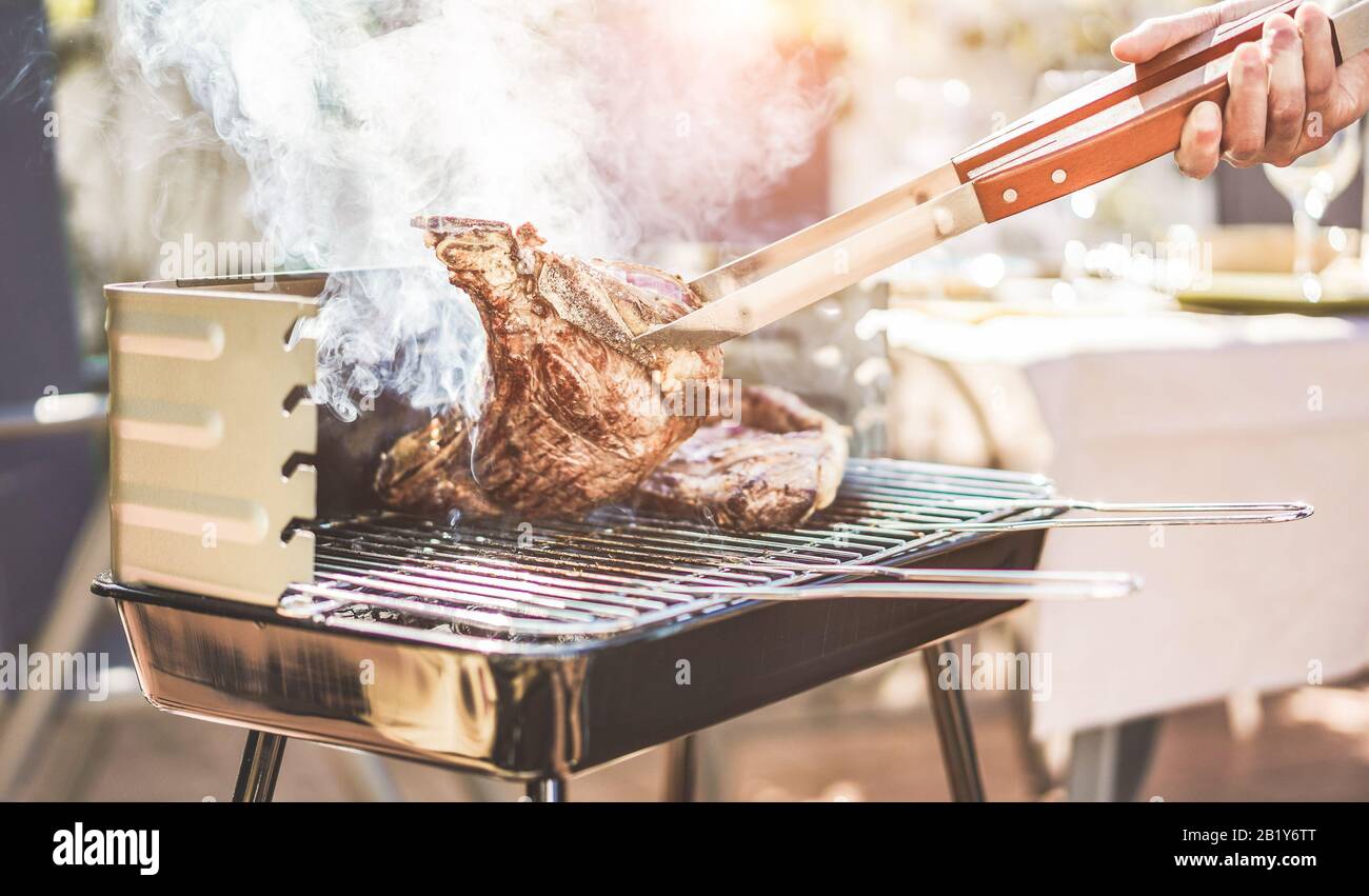 Male chef grill t-bone steak at barbecue dinner outdoor - Man cooking meat for a family bbq meal outside in backyard garden - Summe lifestyle, food an Stock Photo