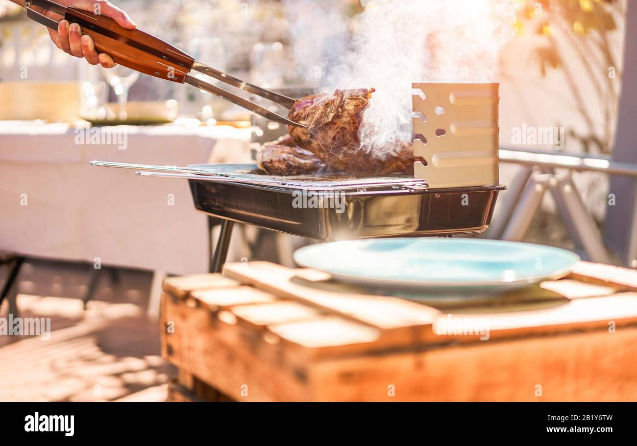 Male chef grill t-bone steak at barbecue dinner outdoor - Man cooking meat for a family bbq meal outside in backyard garden - Summe lifestyle, food an Stock Photo