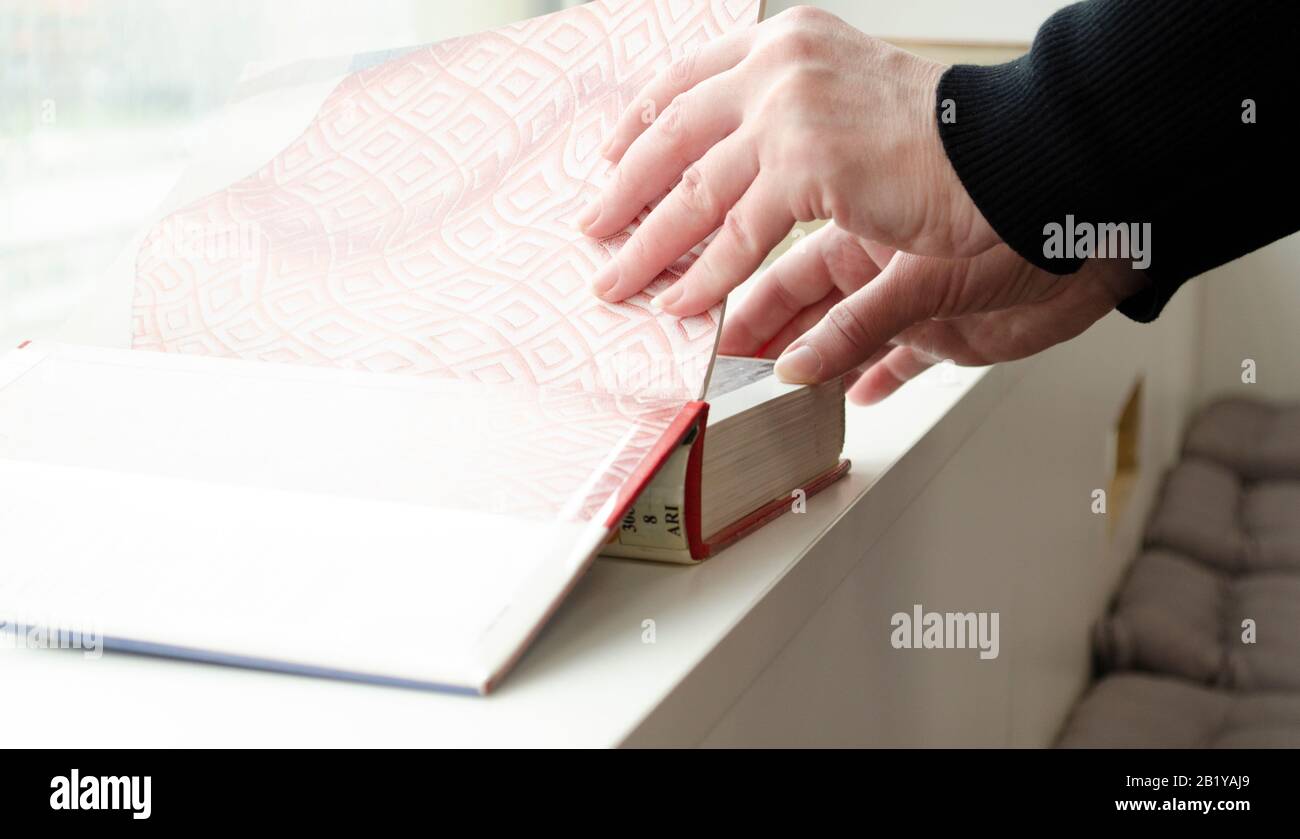 A person reading books near the window. Hands turns over book page. Stock Photo