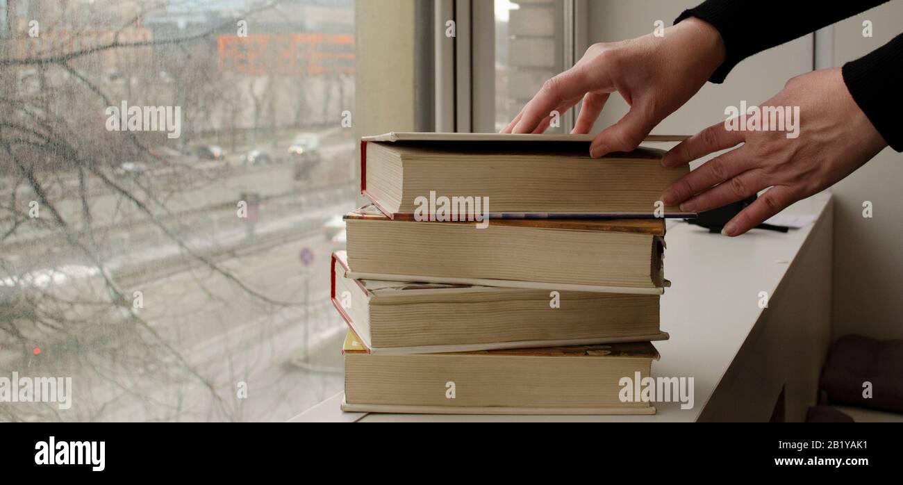 A person reading books near the window. Hands turns over book page. Stock Photo