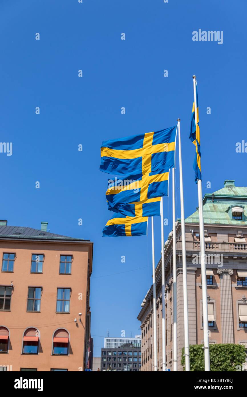 Many flags of Sweden on a metal bar in the air against the background of a building. Clear blue sky Stock Photo