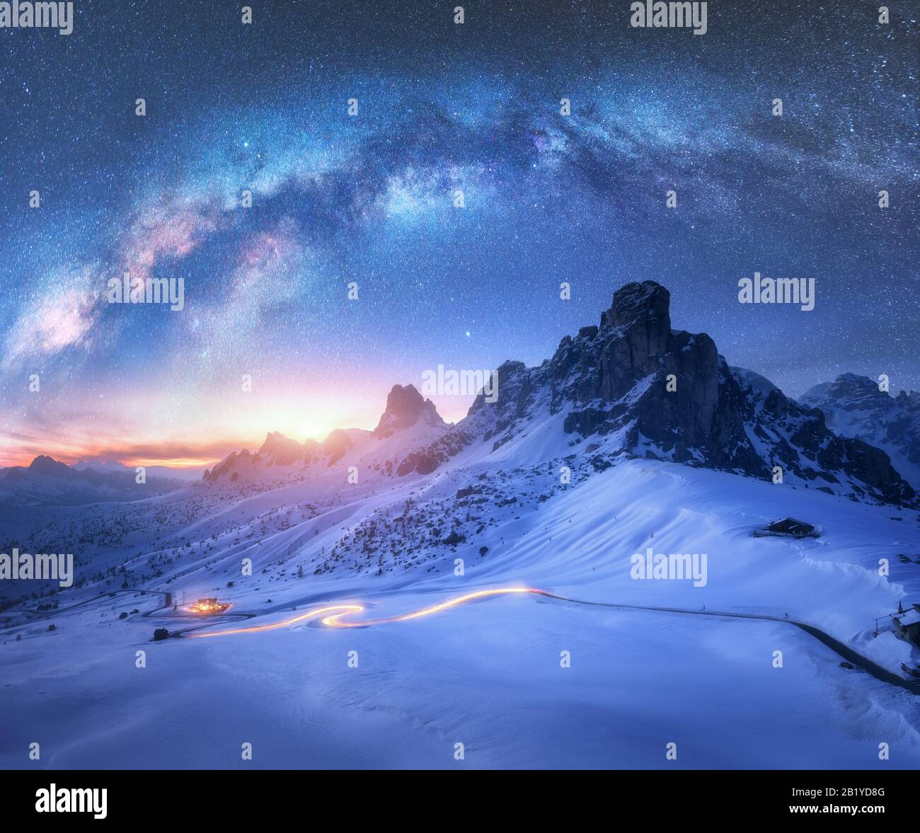 Milky Way over snowy mountains and car headlights on the road Stock Photo