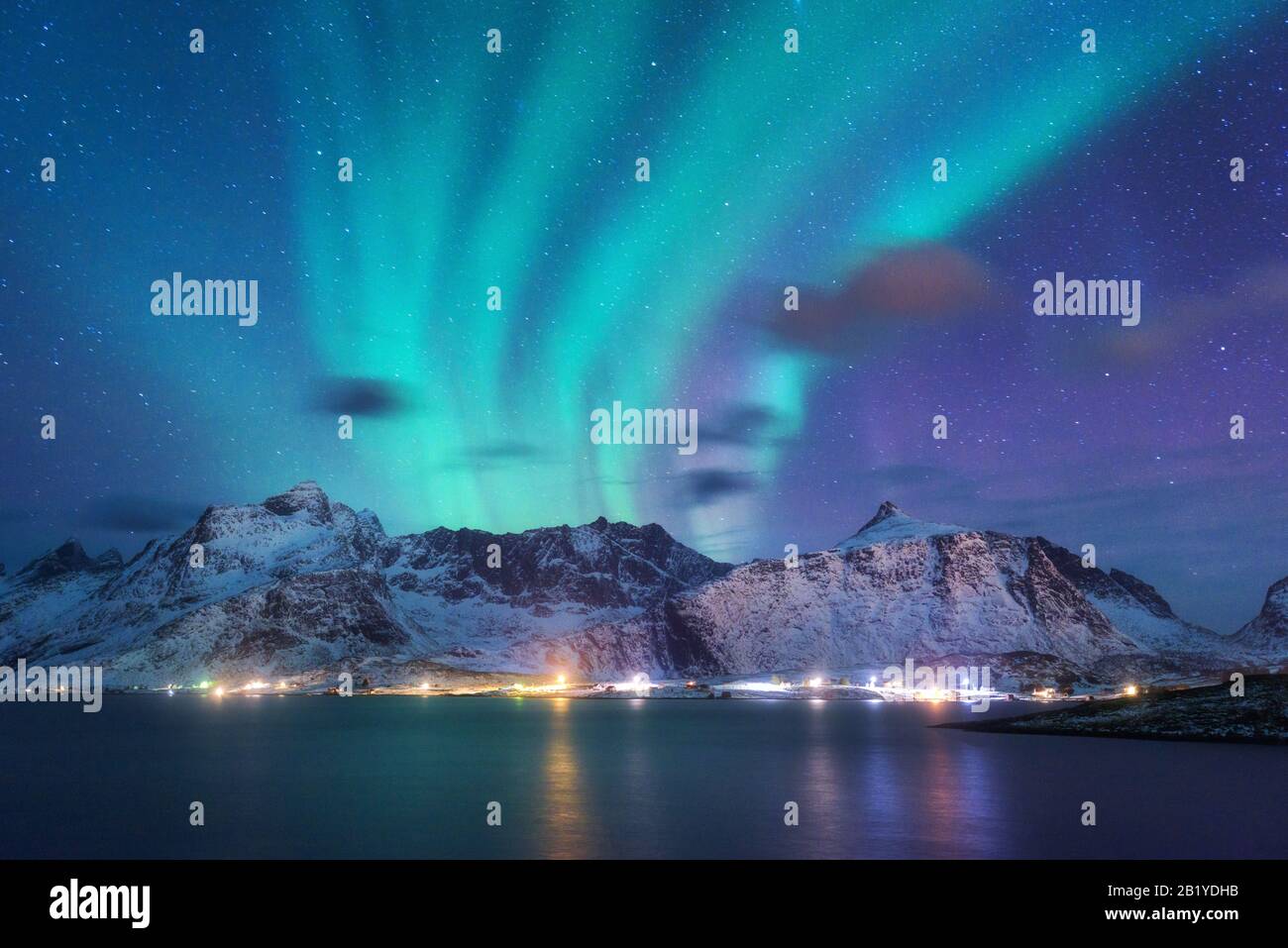 Aurora borealis over the sea, snowy mountains and city lights Stock Photo