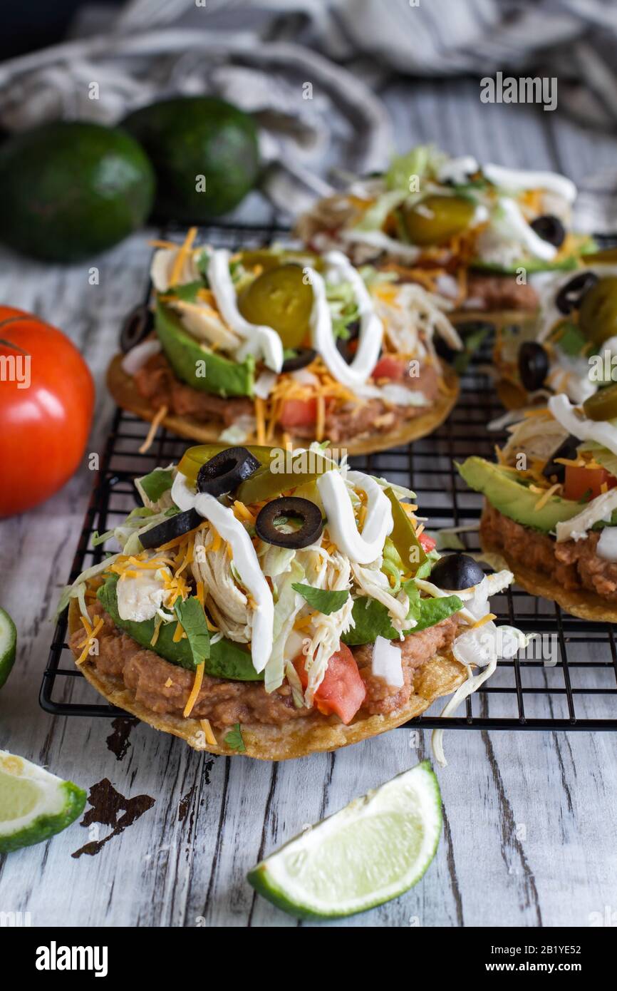 Homemade chicken tostadas with refried pinto beans, fresh cilantro, shredded cheddar cheese, avocados, black olives, sour cream, lettuce, jalapenos, l Stock Photo