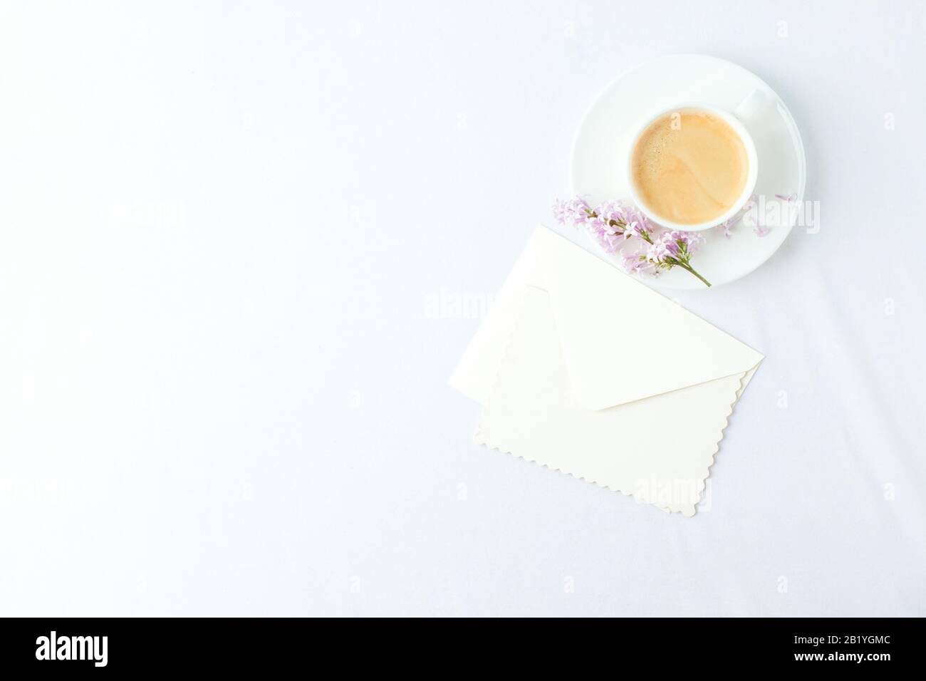 Minimal elegant composition with coffee cup and lilac branches, envelope on white background, female morning breakfast, woman mother day, saint valent Stock Photo