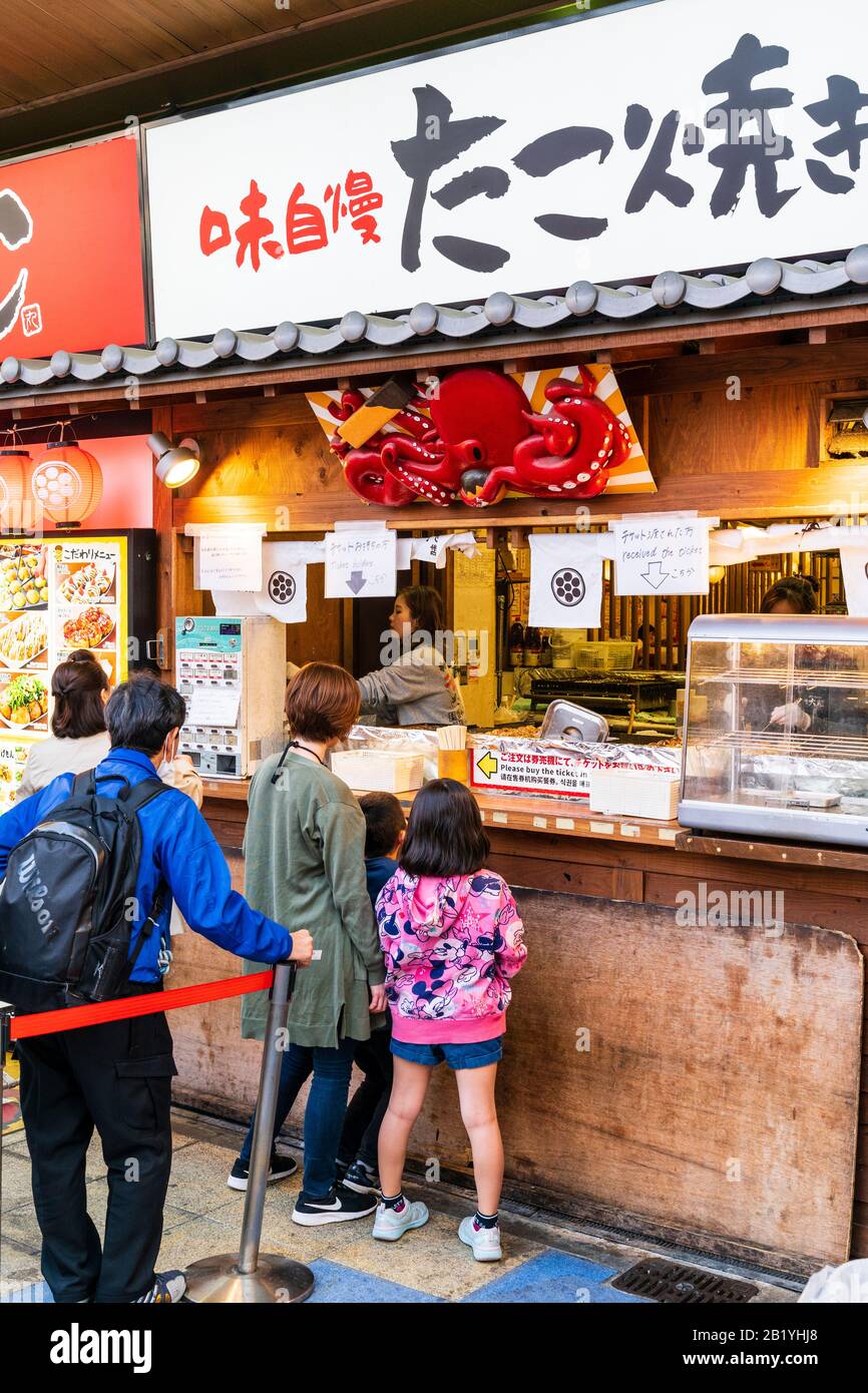 People waiting to be served at takeaway takoyaki counter in Shinsakei, Osaka. Disches are selected by ticket machine and Stock Photo