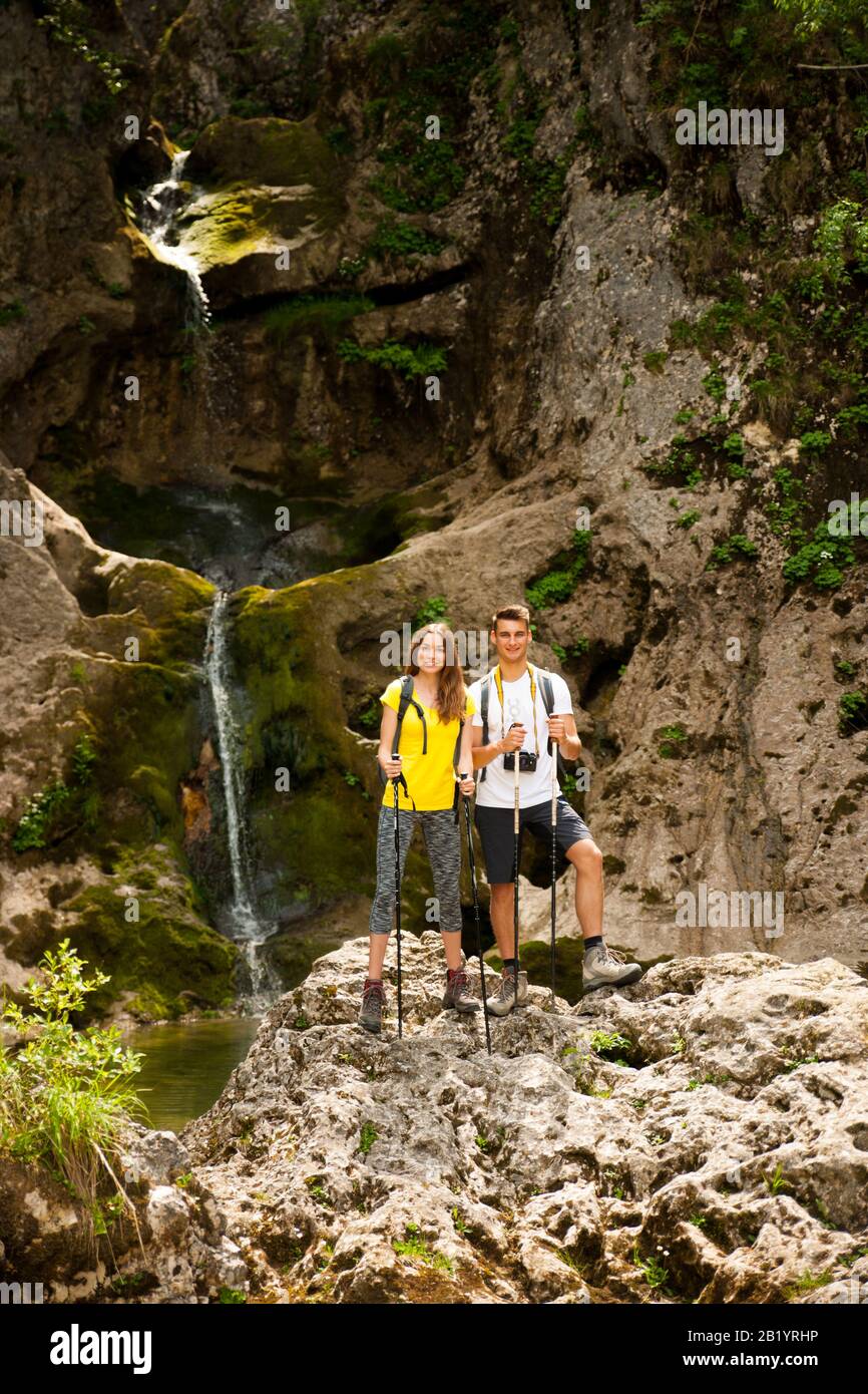 active young couole hiking in nature resting near waterfalll and taking pictures with camera Stock Photo
