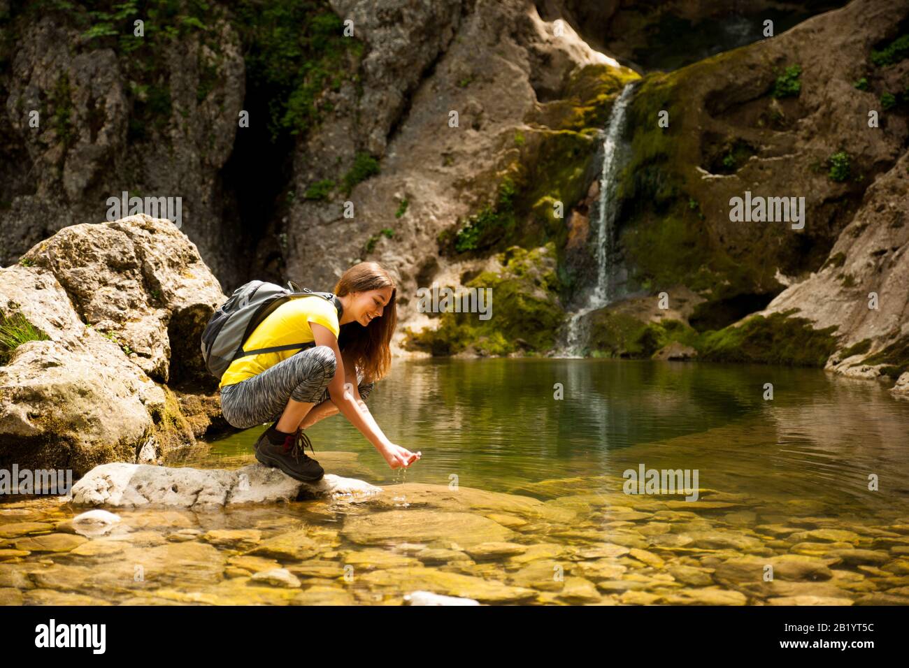 active young woman drinking water from a mountain creek on a warm ...