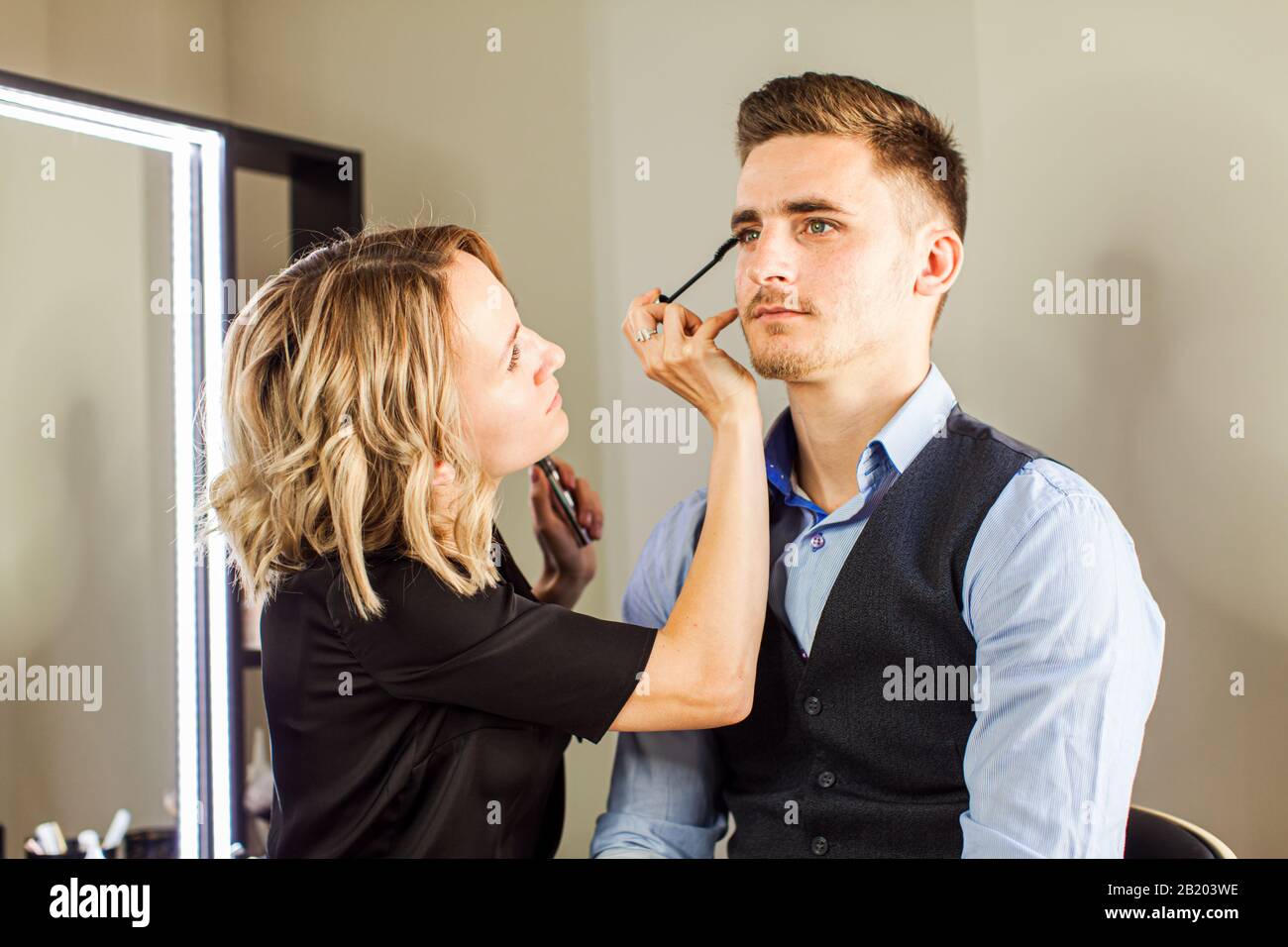 Professional actor preparation before shoot. Handsome young man applying by professional make up of visagist. Stock Photo