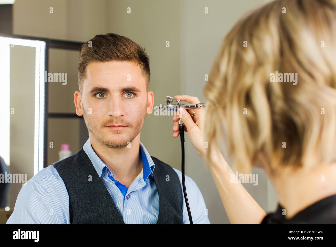 Handsome young man applying by professional make up of visagist. Stock Photo