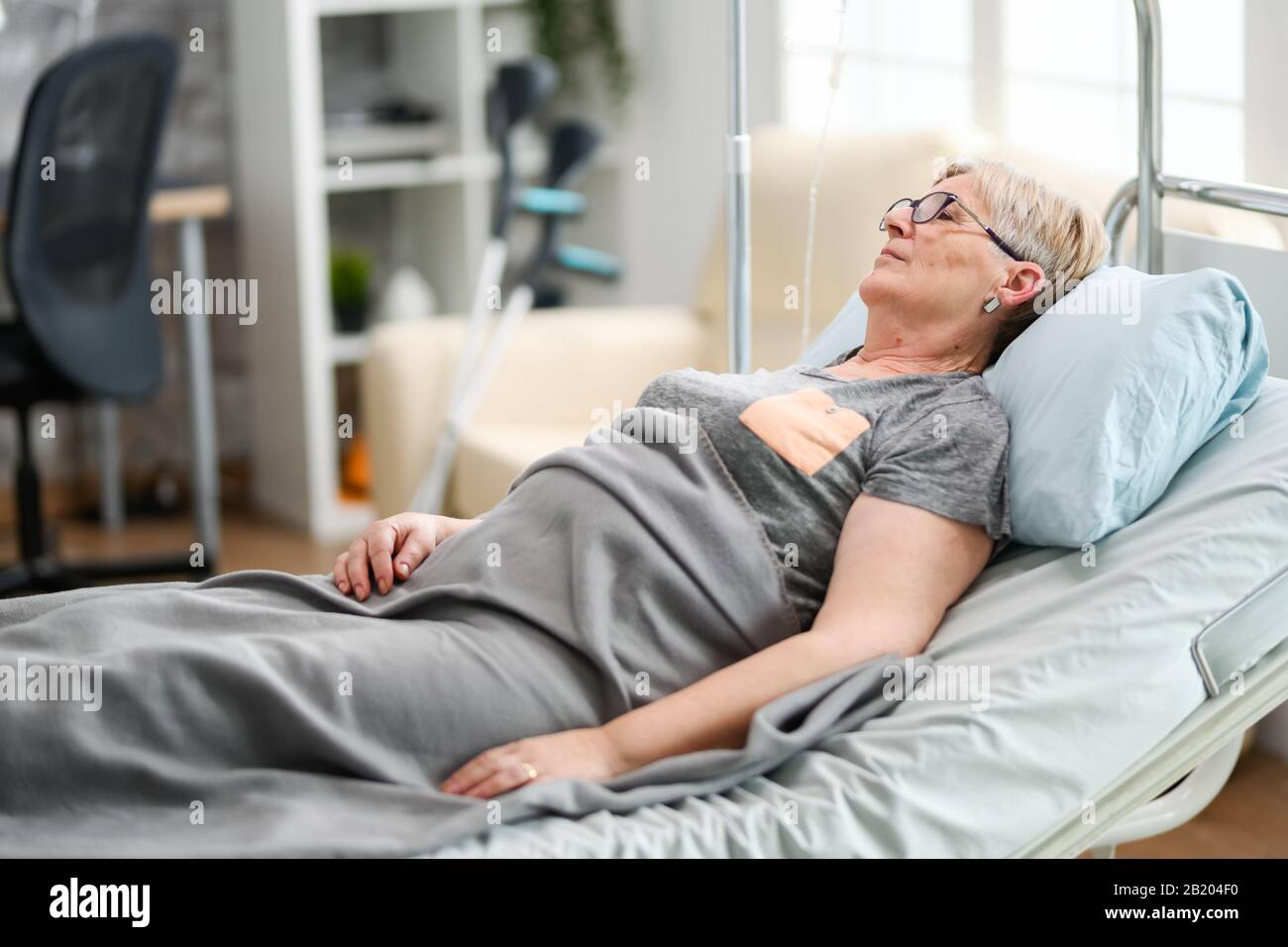 Elderly age woman sleeping in a nursing home bed covered with a blanket