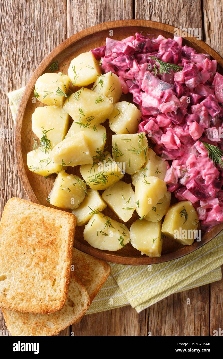 German red herring salad served with boiled potatoes closeup in a plate on the table. Vertical top view from above Stock Photo