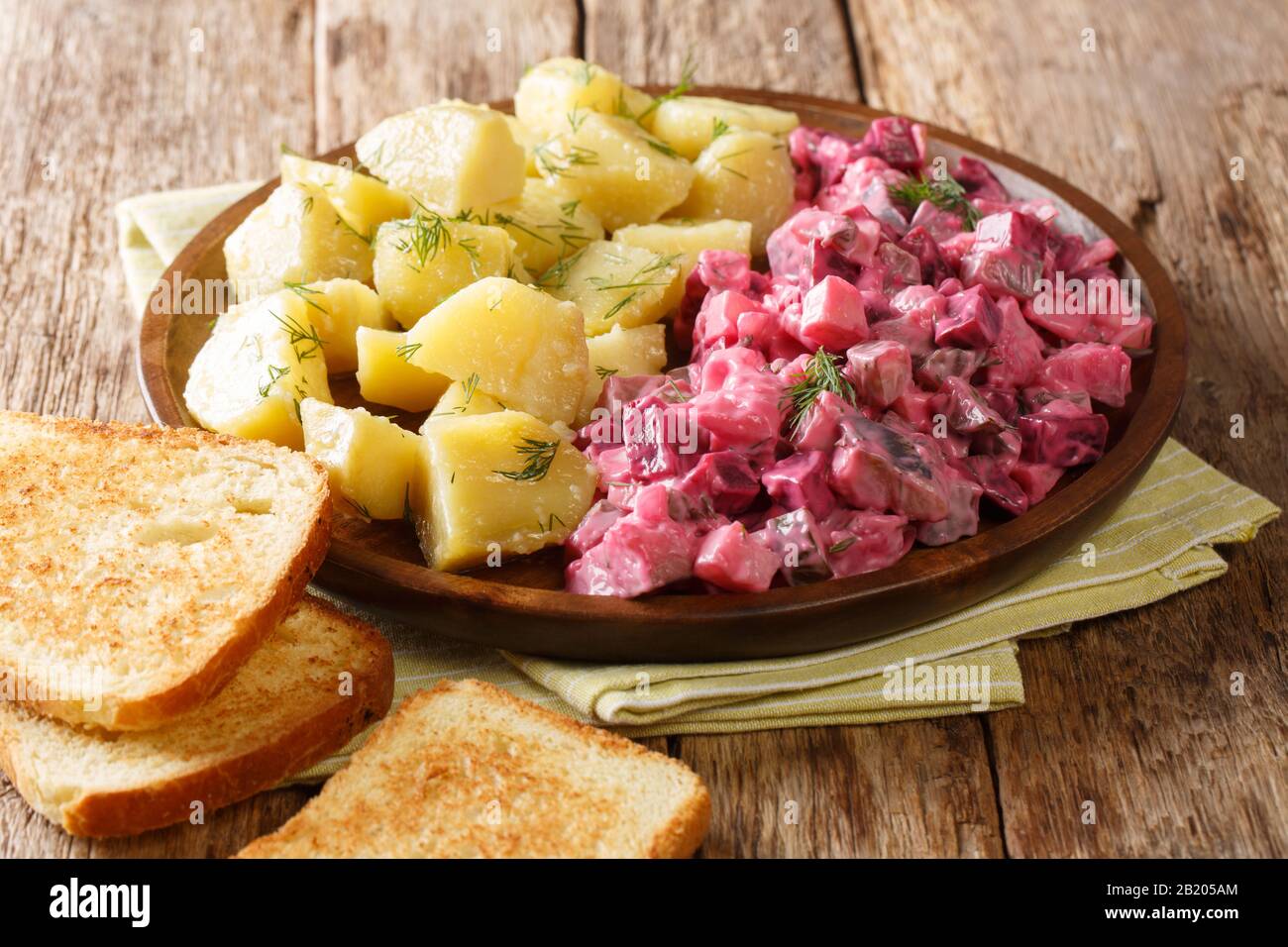 Winter German herring salad with vegetables and a side dish of boiled potatoes close-up in a plate on the table. horizontal Stock Photo