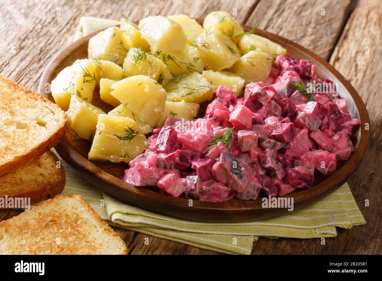 Serving herring salad with vegetables and a side dish of boiled potatoes close-up in a plate on the table. horizontal Stock Photo