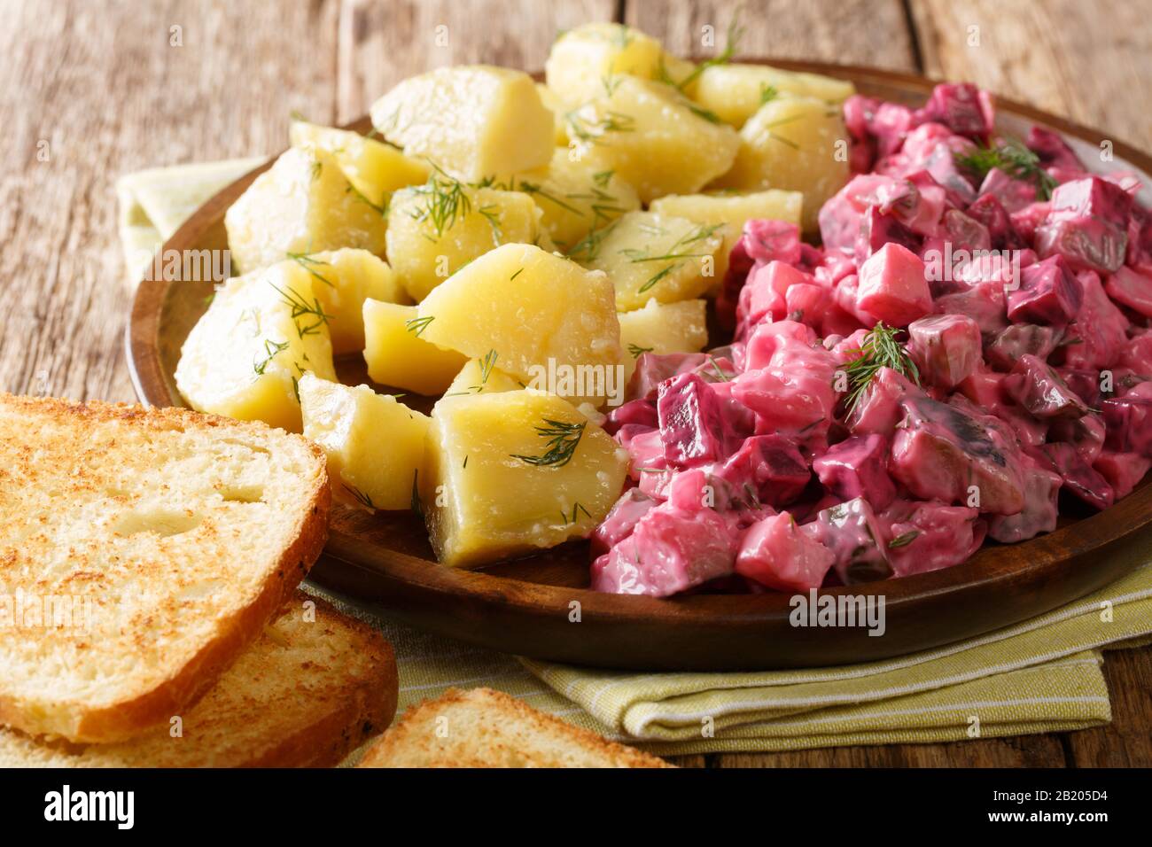 Tasty herring salad with vegetables and a side dish of boiled potatoes close-up in a plate on the table. horizontal Stock Photo
