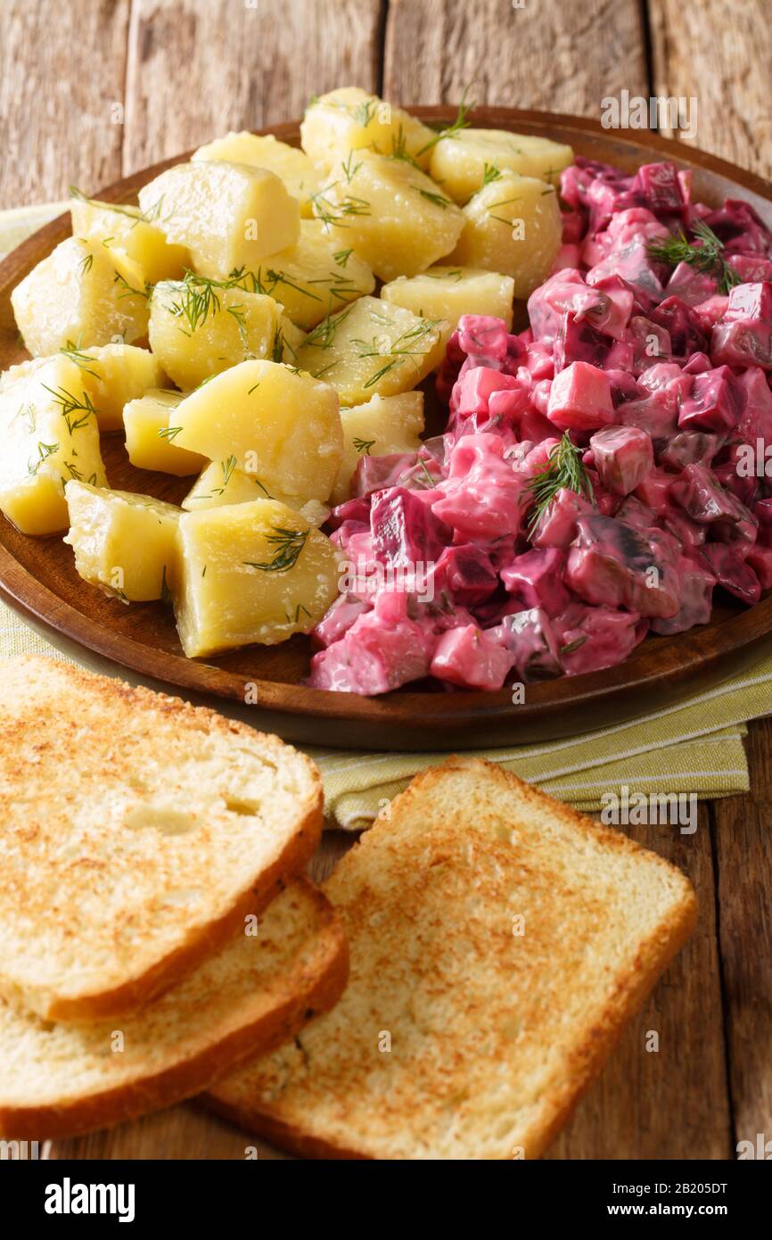 Traditional German red herring salad with garnish of boiled potatoes close-up in a plate on the table. vertical Stock Photo