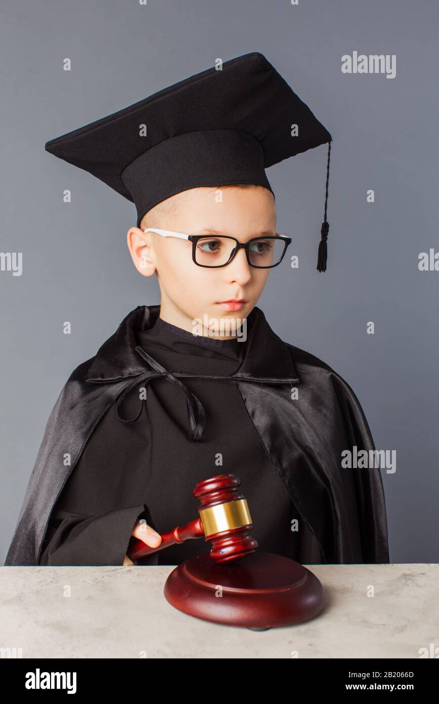 Portrait of serious smart child in graduation cap playing in judge ...