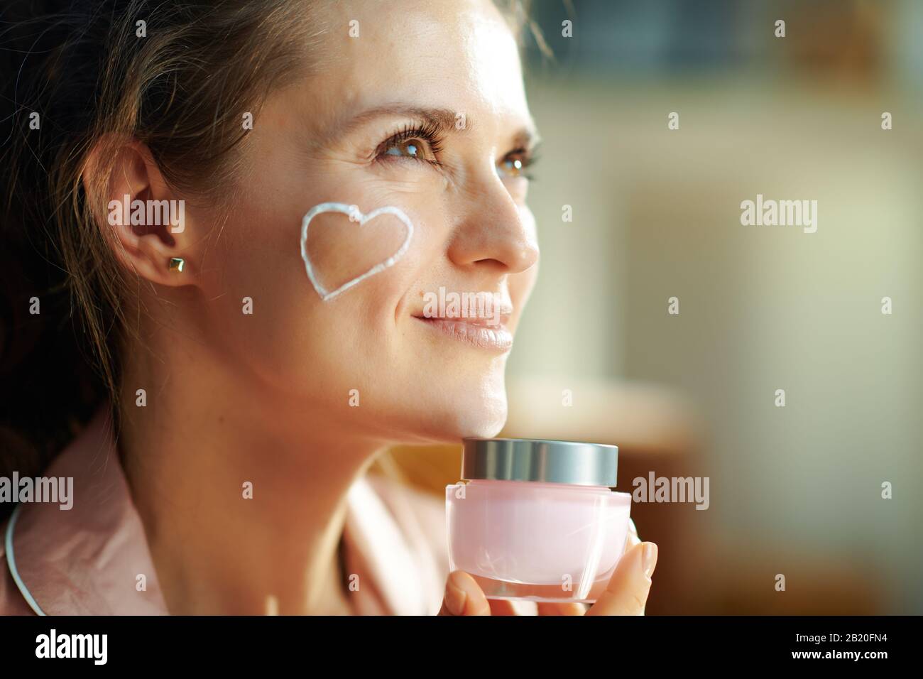 pensive elegant 40 years old woman in pajamas with white facial cream